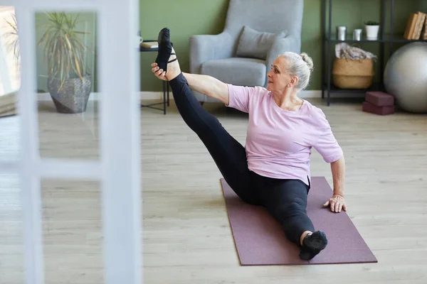 Senior donna attiva seduta sul tappeto e fare esercizio di stretching — Foto Stock