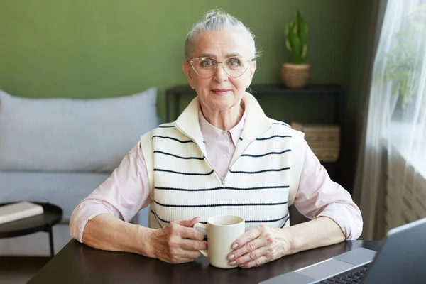 幸せな成熟した女性で眼鏡とカジュアルな服を持っているお茶byテーブル — ストック写真