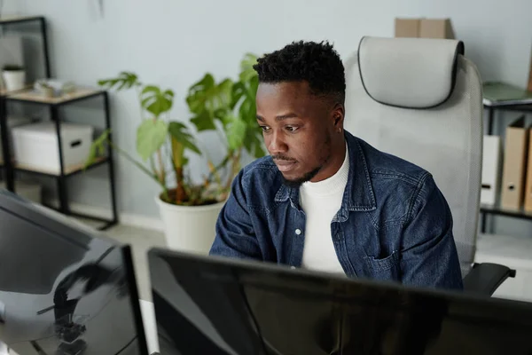 Giovane uomo nero in abiti casual seduto davanti ai monitor del computer — Foto Stock