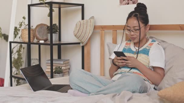 在她的房间里 一个喜欢在智能手机上滚动和在床上使用笔记本电脑的小工具的亚洲少女的中景照片 — 图库视频影像