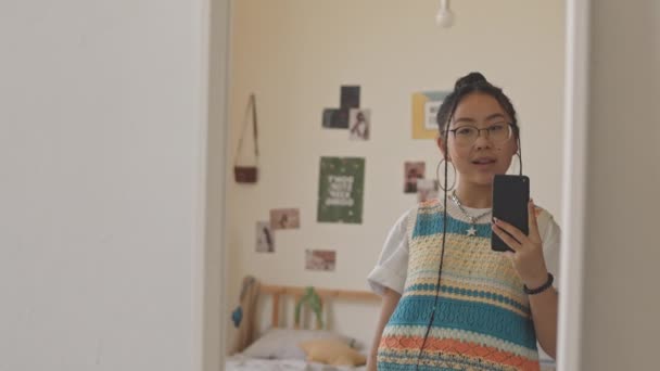 身着时髦服装和眼镜的亚洲少女在镜子前的智能手机上自拍照时出现V字形的中影 — 图库视频影像