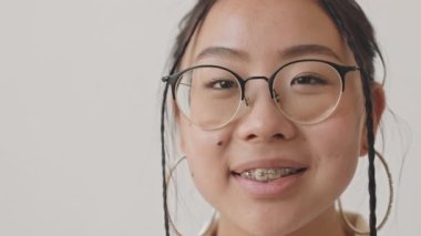 Gözlüklü gülümseyen Asyalı genç kızın yakın plan portresi beyaz arka planda duran kameraya bakıyor.