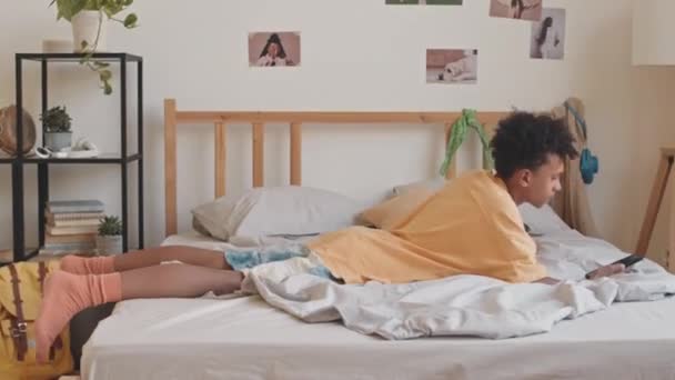 Pan Shot Gen Biracial Teenage Boy Jumping His Bed Smartphone — Stock Video