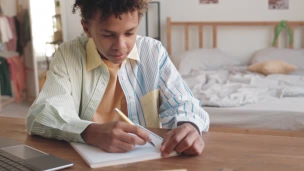 Stab Wide UpショットのBiracial十代の男の子でカジュアルウェア取るノートでコピーブックに家で勉強しながら使用ノートパソコン — ストック動画