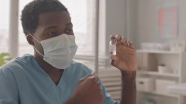 Ofisinde hastasıyla konuşurken elinde küçük bir aşı şişesi olan yüzü maskeli Afrikalı Amerikalı bir doktorun yavaş çekimleri.