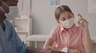 Maskeli 13 yaşında, beyaz bir kızın aşıyı şişede tutarken Afrika kökenli Amerikalı bir doktorla aşının faydaları hakkında konuşurken çekilen belden aşağısı.