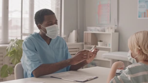 中慢镜头的蒙面年轻非裔美国医生和白人小男孩在预约期间谈论疫苗接种 — 图库视频影像