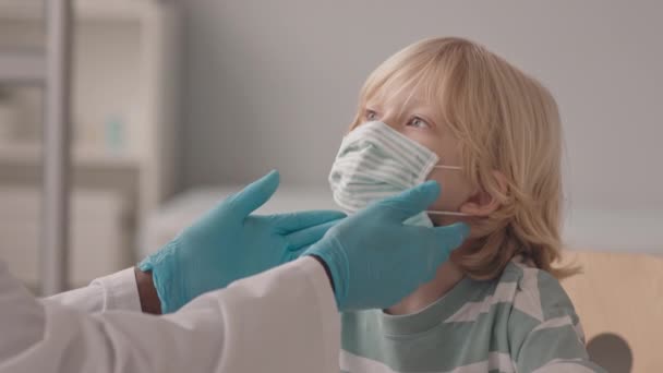 医師事務所で予約している顔マスク姿の白人少年のスローモとの中級クローズアップ リンパ節の検査をしている — ストック動画