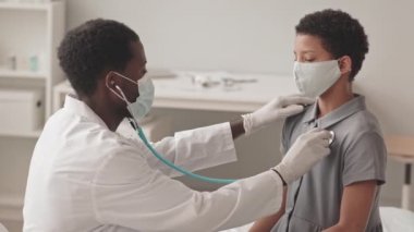 Afrika kökenli Amerikalı bir doktorun steteskoplu Afro-Amerikalı bir kızın kalbini dinlediği belden aşağısı. İkisi de maske takıyor.