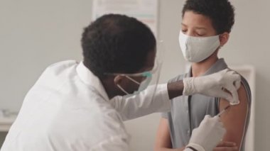 Afrika kökenli Amerikalı erkek doktorun, Covid-19 aşısını yaptıktan sonra Afrika kökenli Amerikalı bir kızın omzuna yara bandı yapıştırdığı yavaş çekim.