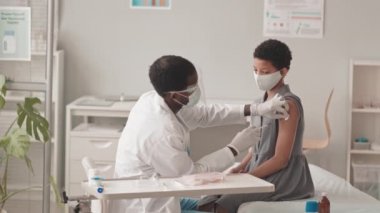 10 yaşındaki Afro-Amerikan bir kızın modern doktorların ofisinde Covid-19 aşısı olurken orta yavaş çekimleri.