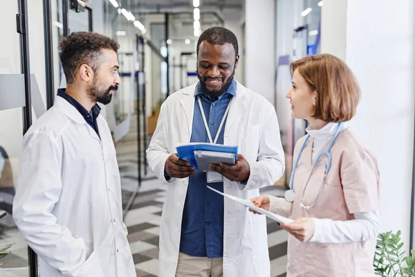 Heureux jeune clinicien afro-américain regardant à travers la forme médicale du patient — Photo