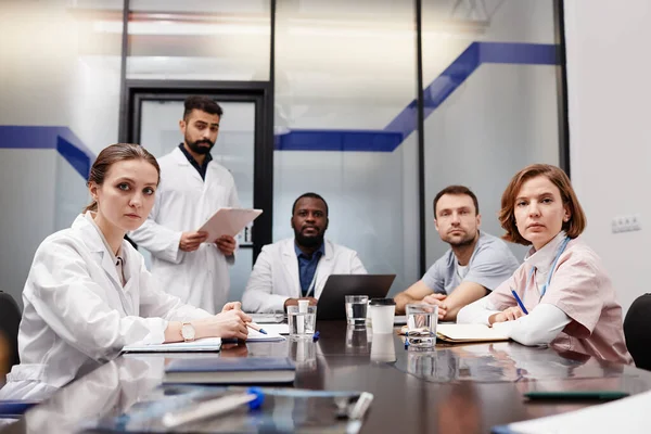 Interkulturális orvosi szakértők csoportja az asztalnál ülő laborköpenyekben — Stock Fotó