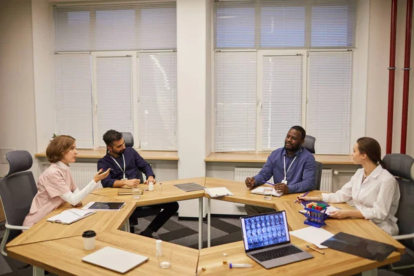 Quatro jovens especialistas contemporâneos sentados à mesa redonda durante a discussão — Fotografia de Stock