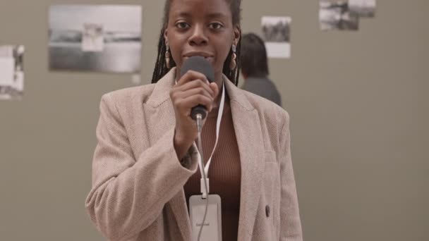 年轻的非洲裔美国女导游一边看着相机一边用麦克风谈论当代艺术画廊里的抽象照片 这让人提心吊胆 — 图库视频影像