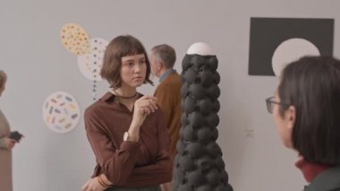 Modern sanat müzesindeki sergi sırasında çeşitli gençlerin kavramsal sanat objelerini tartışıp incelediği orta yavaş bir çekim.