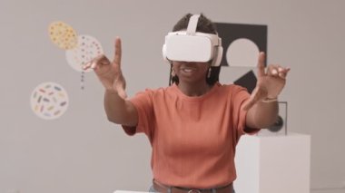 Modern sanat müzesindeki sanal gerçeklik sergisi sırasında VR kulaklıklı genç Afro-Amerikan kadının orta yavaş çekimleri.
