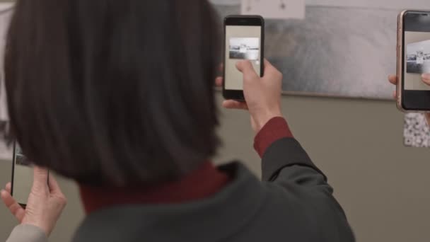 写真を撮るスマートフォンを持つ観光客のグループの後方ビューのスローモーション現代美術館の壁にかかっているフレーム内の抽象的な黒と白の写真 — ストック動画