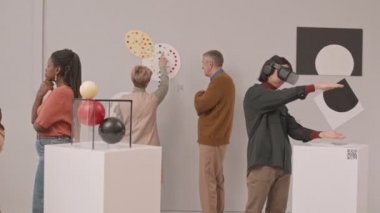 Çağdaş sanat müzesindeki sergi sırasında kavramsal sanat objelerini inceleyen bir grup insanın orta yavaş çekimi. Genç adam kulaklık takıyor.