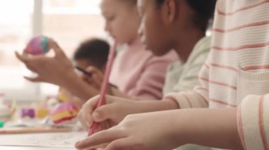 Paskalya temalı renklendirme sayfasında resim çizen Kafkasyalı yakışıklı sarışının yavaş çekimleri sırasında çok ırklı arkadaşları paskalya yumurtalarını birlikte masaya oturtup nefes nefese kalıyorlar.