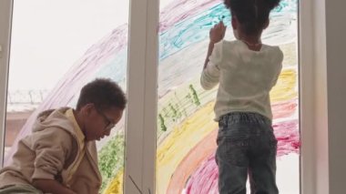 Pencereye gökkuşağı çizen komik Afro-Amerikan kardeşlerin yavaş çekimi