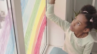 Pencereye gökkuşağı çizen Afro-Amerikalı bir oğlan ve kız birlikte pencere kenarında oturuyorlar.