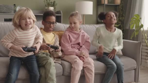 Közepes Lassú Négy Örömteli Többnemzetiségű Gyerekek Szórakozás Videojátékok Együtt Kanapén — Stock videók