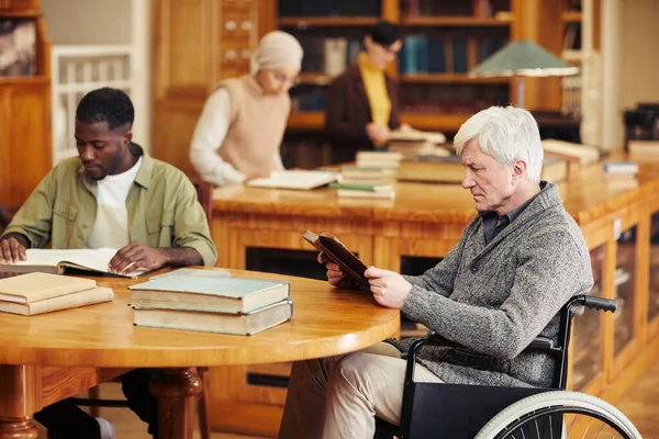 Hombre mayor en silla de ruedas en la biblioteca —  Fotos de Stock