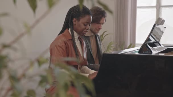 若い白人男性教師と個々の音楽レッスンでピアノ演奏を練習若い才能アフリカ系アメリカ人女性の中低速 — ストック動画