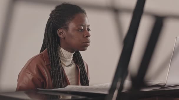 ウエストアップ遅いの若いですアフリカ系アメリカ人女性学習するためにピアノを演奏するオンラインビデオレッスンをノートパソコンで勉強音楽ノートと一緒に先生 — ストック動画