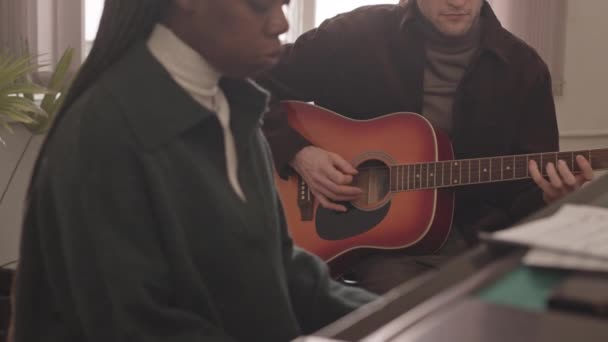 在室内排练的年轻的跨种族音乐二重唱的慢镜头 白人男子弹吉他 非洲裔美国妇女弹钢琴 — 图库视频影像