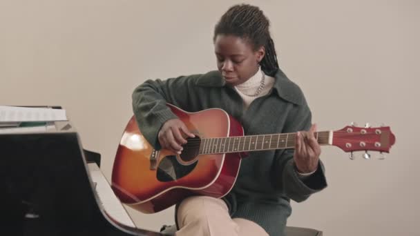 中等速度的年轻黑人妇女在附近的钢琴键盘上弹奏吉他 并在智能手机上录音 — 图库视频影像