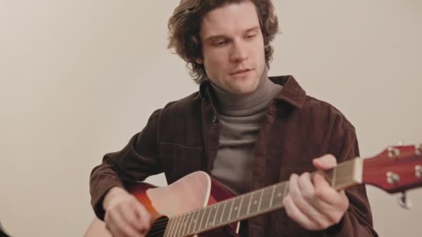 中等速度的年轻英俊白人男子独自坐在室内弹吉他 — 图库视频影像