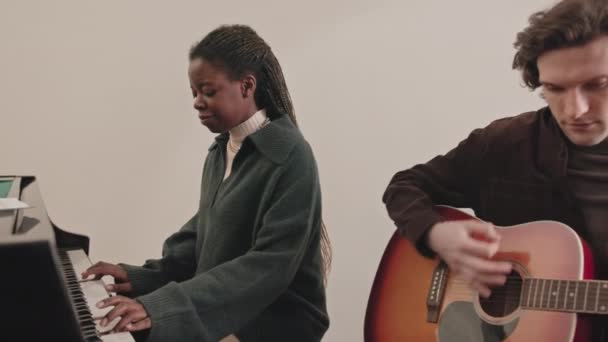 中等速度的年轻的跨种族音乐夫妇在室内排练 非洲裔美国妇女弹钢琴 白人男子弹吉他 — 图库视频影像