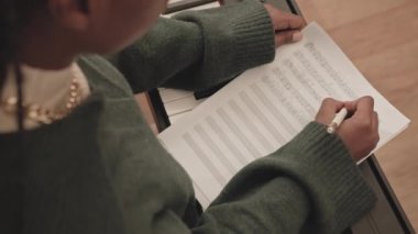 Afrika kökenli Amerikalı kadın söz yazarının, klavye için yeni bir şarkı yaratırken kağıda notalar yazmasının yavaş görüntüsü.