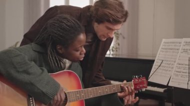 Erkek öğretmenin ona yardım ettiği müzik dersinde akustik gitar çalmayı öğrenen Afro-Amerikan genç bir kadının orta yavaşlığı.