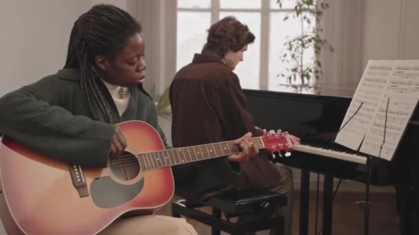 中等速度的年轻的跨种族音乐夫妇一起在室内演奏 非裔美国妇女在背景音乐中弹吉他 白人男子在背景音乐中弹大钢琴 — 图库视频影像