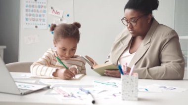 Beyaz sınıf bayan öğretmeniyle ders sırasında 5 yaşındaki akıllı Afro-Amerikan alfabesinin öğrenme harflerini yavaş yavaş bele al.