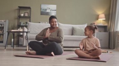 Afrika kökenli Amerikalı genç bir kadın ve 5 yaşındaki güzel kızı evde yoga minderinde birlikte meditasyon yapıyorlar.
