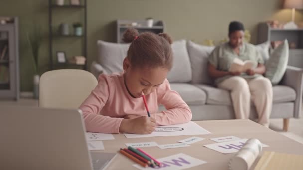 ウエストアップSlomoの5歳アフリカ系アメリカ人ゲンA女の子勉強文字と着色でページに座っていますホームで彼女のお母さん読書本でバックグラウンド — ストック動画