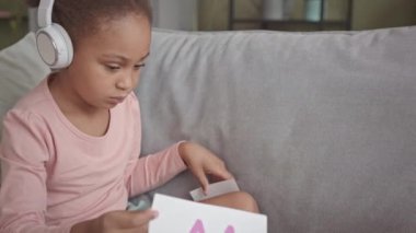 Orta boy Afro-Amerikan gen kulaklıklı bir kız alfabe öğrenirken evde bilgisayarından video dersi alıyor.