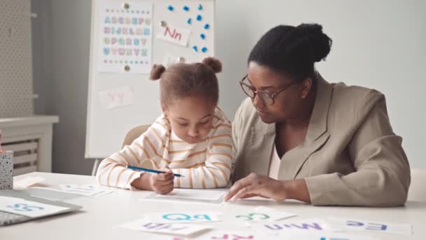 アフリカ系アメリカ人の就学前の少女と女性教師が教室で授業中に英語のアルファベットを学ぶ — ストック動画