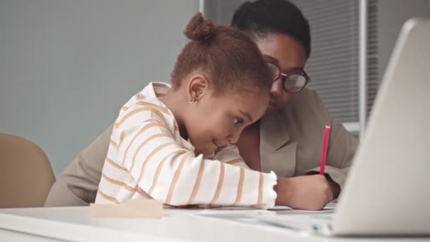 英語のアルファベットを練習しながら 彼女を助ける女性教師と一緒に紙の上に書くアフリカ系アメリカ人の少女 — ストック動画