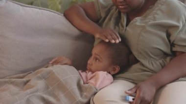 Siyahi kadının hasta çocuğuna bakması. 5 yaşında termometreyle kanepenin altında yatıyor.