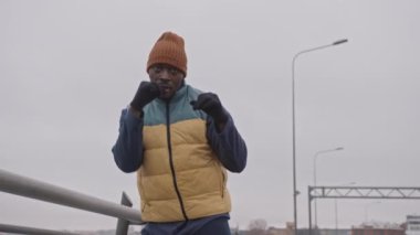 Sıcak giyimli kararlı bir Afro-Amerikalı, soğuk bir sabahta dışarıda boks antrenmanı yapıyor.