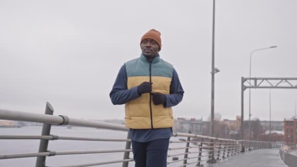 寒冷的早晨 穿着保暖运动服沿着桥慢跑的非洲裔美国人的中等速度 — 图库视频影像