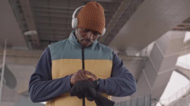 Soğuk bir sonbahar sabahı dışarıda koşarken akıllı saatinin ayarlarını ayarlayan kulaklıklı Afro-Amerikalı bir adam.