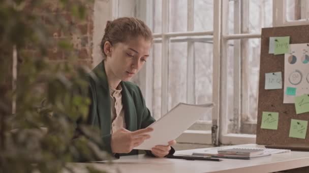 自信のある若い白人のビジネスマンの中低速ロフトスタイルのオフィスでデスクに座ってビジネス文書を扱う女性 — ストック動画