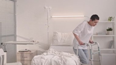 Hastane koğuşunda ameliyat sonrası ayakta durmak için Walker kullanan olgun, beyaz bir kadın.