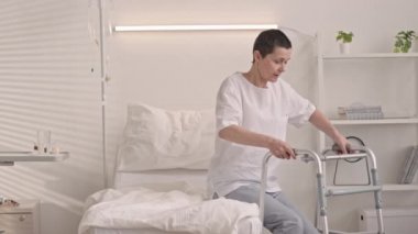 Yetişkin, beyaz bir kadının, aylakları kullanarak hastane yatağından kalkması ve ameliyat sonrası rehabilitasyon dönemi geçirmesi.